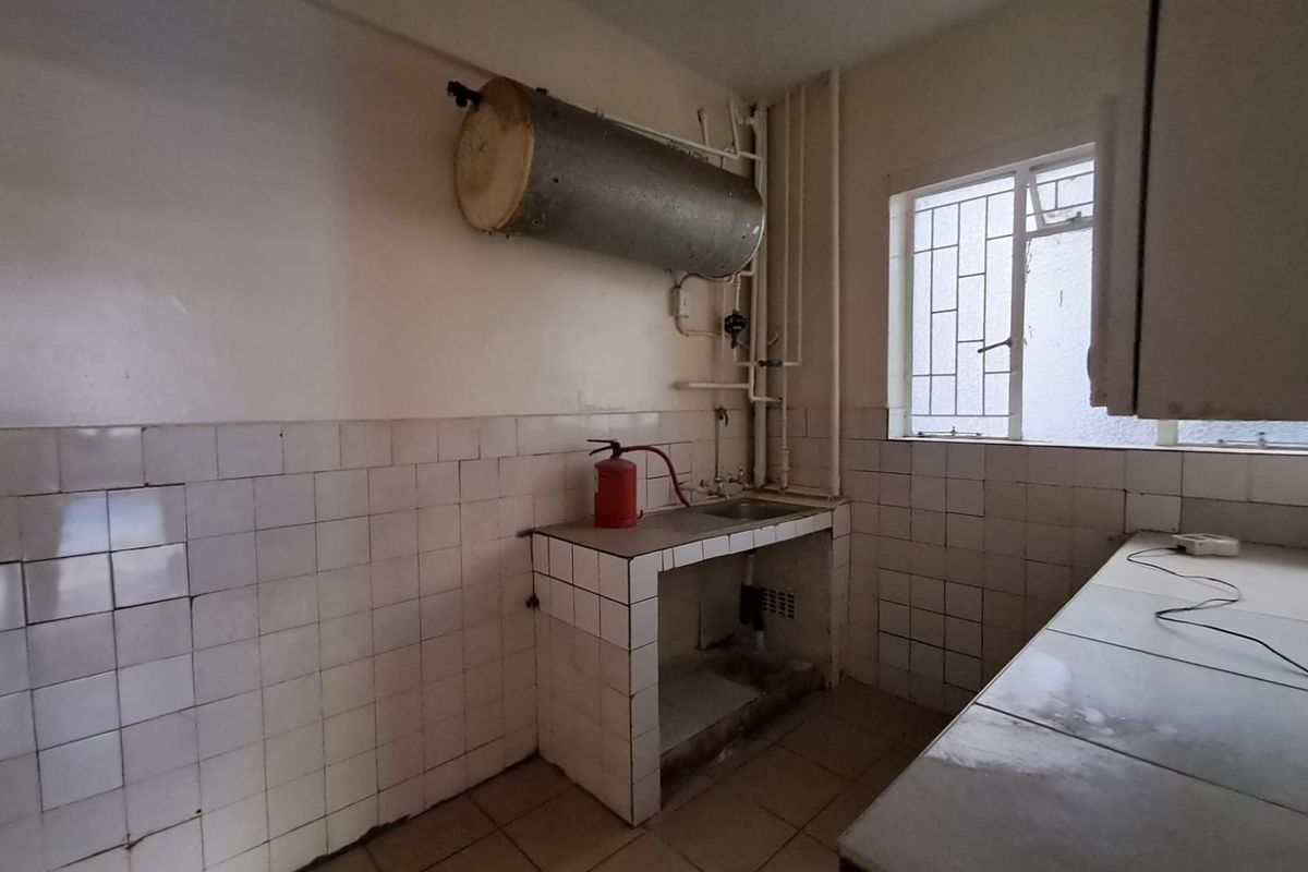 A dated kitchen area featuring tiled surfaces, a stainless steel sink, and an exposed electric water heater, requiring significant renovation and modernization.
