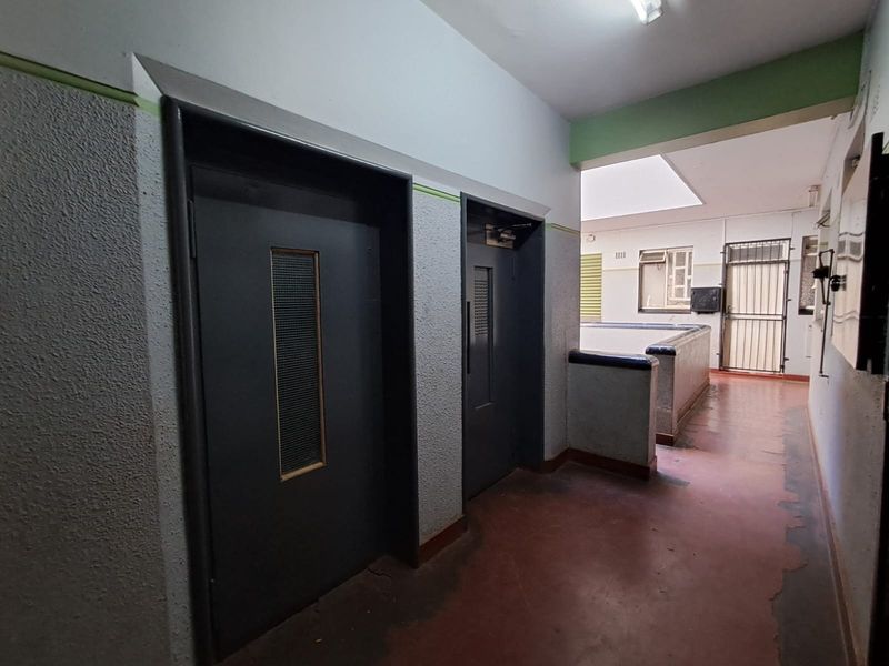 A communal apartment hallway featuring elevator access, a security gate, and a skylight, showing signs of wear on the flooring and walls.