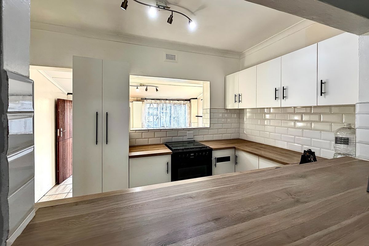 A clean, modern kitchen featuring white cabinetry, subway tile backsplash, wooden countertops, and a breakfast bar overlooking the adjacent living space.