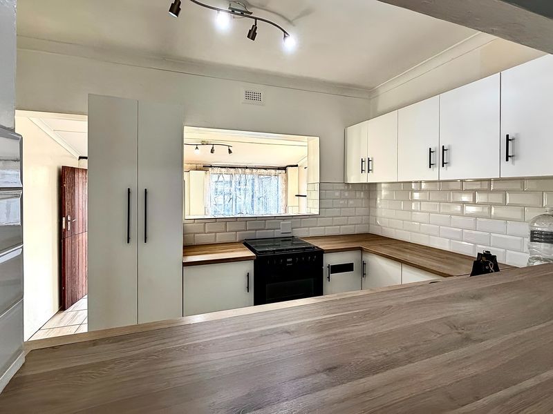 A clean, modern kitchen featuring white cabinetry, subway tile backsplash, wooden countertops, and a breakfast bar overlooking the adjacent living space.