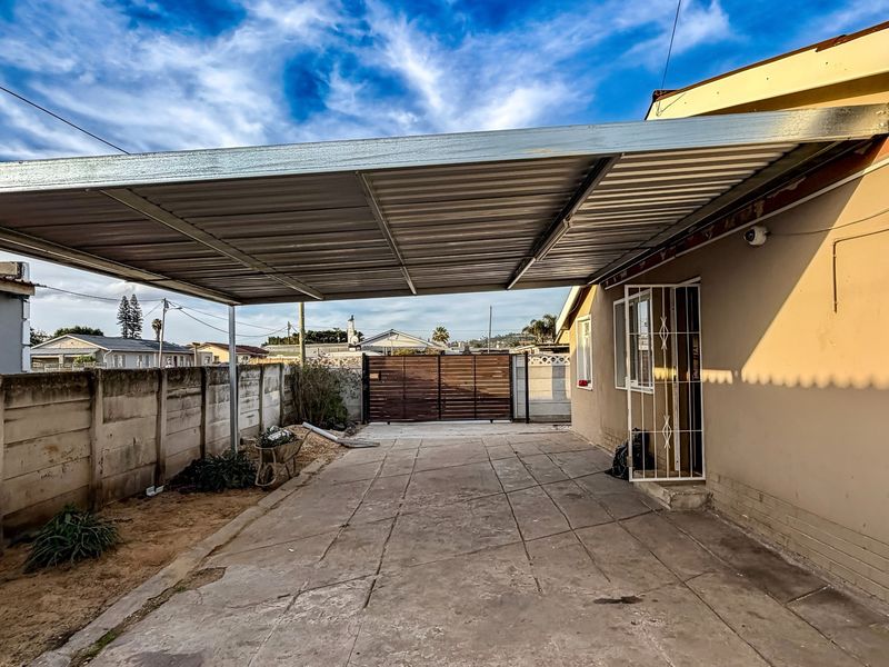 Exterior view of the property featuring a covered carport, concrete driveway, and secure perimeter wall with a gate.