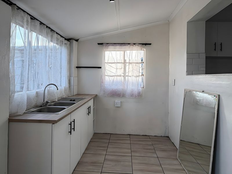A functional kitchen area featuring built-in base cabinetry, a double bowl stainless steel sink, and tiled flooring, ready for modern updates.