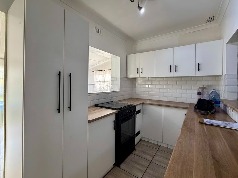 A functional kitchen featuring white cabinetry, subway tile backsplash, wood-look countertops, and a black freestanding oven, with a pass-through window to the adjacent room.
