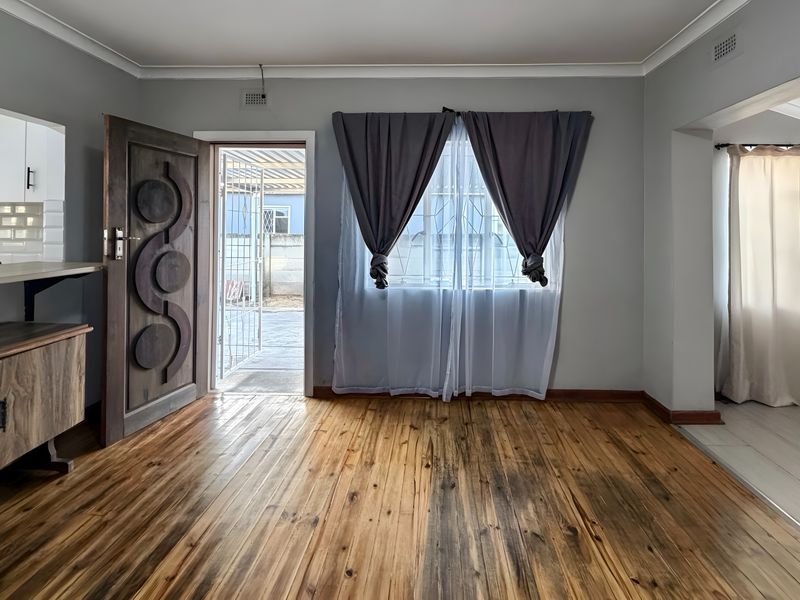 Open plan living area featuring hardwood flooring, built-in kitchen cabinetry with subway tile backsplash, and direct access to the exterior via a security gate.