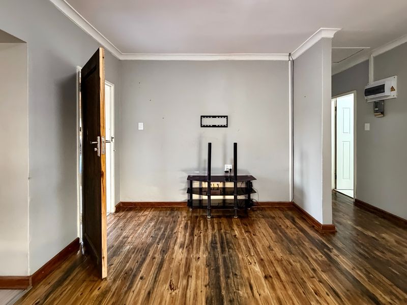 An empty living room featuring laminate wood flooring, coving, and neutral wall finishes, providing a blank canvas for interior design.