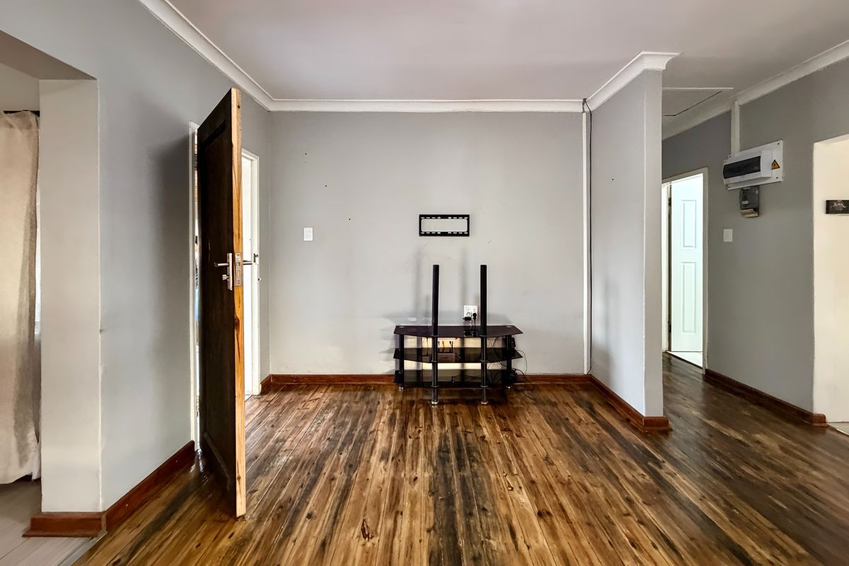 An empty living room featuring laminate wood flooring, coving, and neutral wall finishes, providing a blank canvas for interior design.