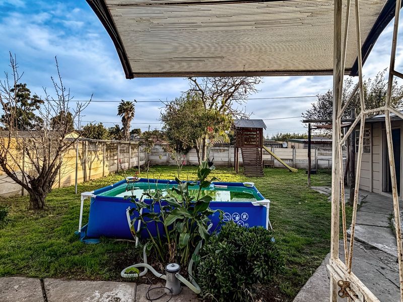 Rear garden area featuring a paved patio with a covered structure, enclosed by concrete boundary walls and including a lawn space.