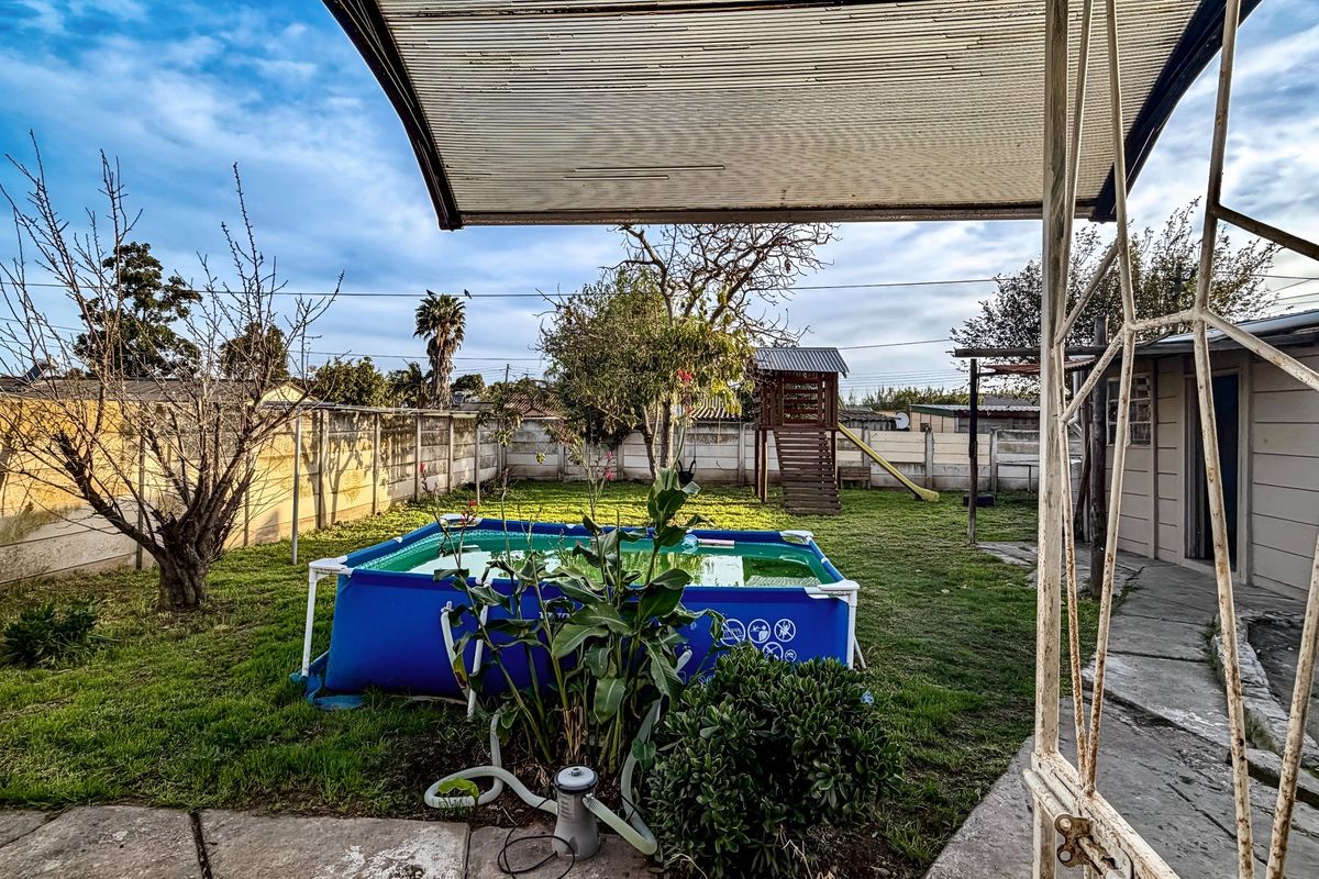 Rear garden area featuring a paved patio with a covered structure, enclosed by concrete boundary walls and including a lawn space.