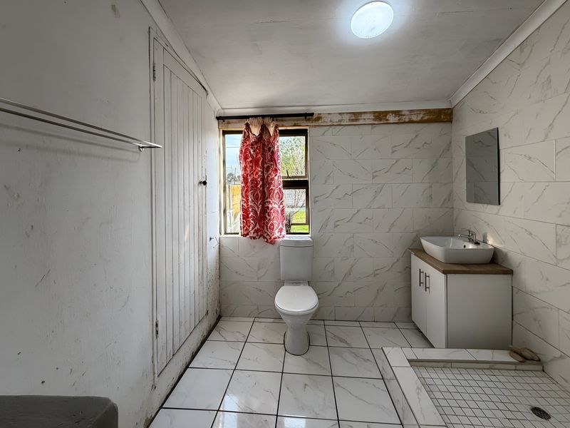 A functional bathroom featuring marble-look wall tiles, a modern vessel sink vanity, and a tiled shower base, currently requiring some cosmetic maintenance.