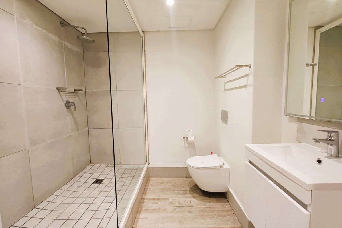 Modern bathroom featuring a spacious walk-in shower with glass screen, wall-mounted toilet, and a sleek vanity unit with basin.