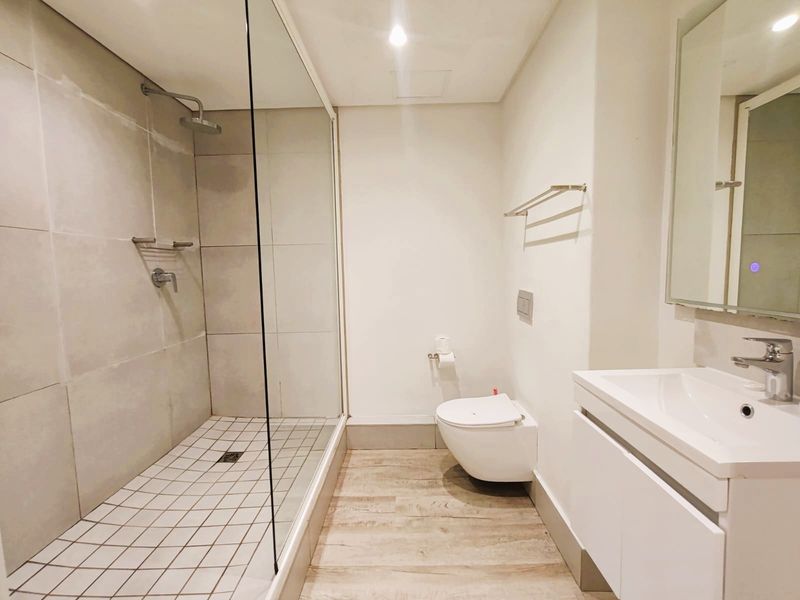 Modern bathroom featuring a spacious walk-in shower with glass screen, wall-mounted toilet, and a sleek vanity unit with basin.