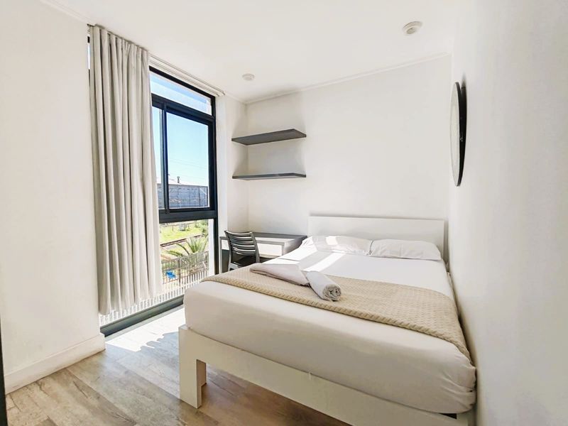 A bright and modern bedroom featuring laminate flooring, built-in shelving, and a large window providing natural light.