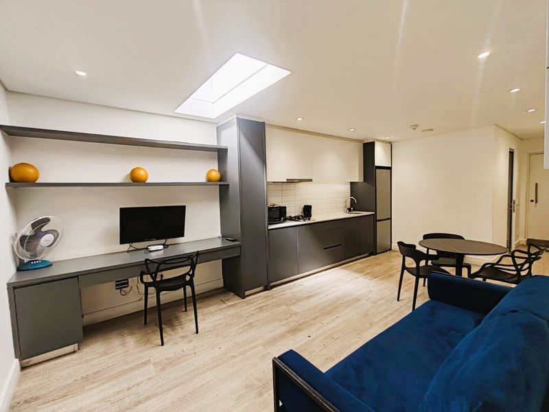 Modern open-plan living area featuring a sleek kitchen with integrated cabinetry, a built-in study nook with shelving, and a bright skylight.