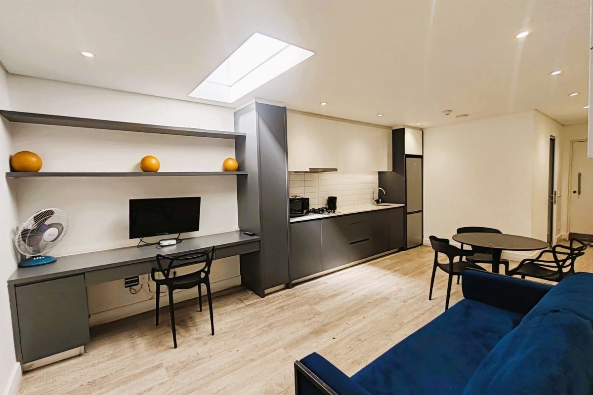 Modern open-plan living area featuring a sleek kitchen with integrated cabinetry, a built-in study nook with shelving, and a bright skylight.