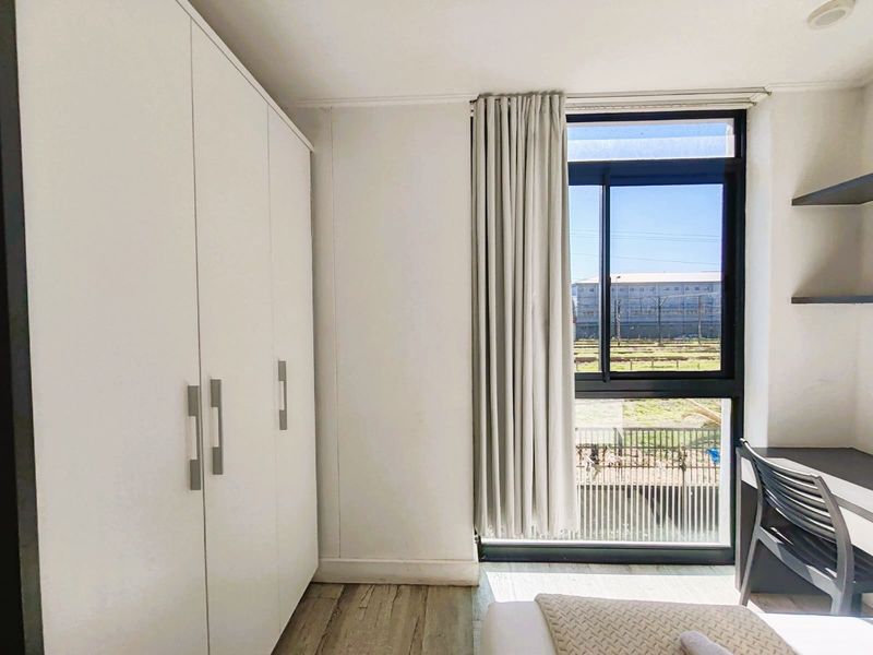 A bright bedroom featuring modern laminate flooring, a large built-in wardrobe, and a window with views of the surrounding area.