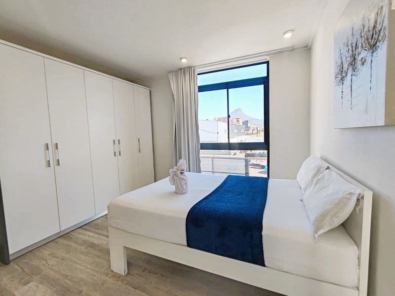 A bright bedroom featuring built-in wardrobes, light laminate flooring, and a window with views of the surrounding area.