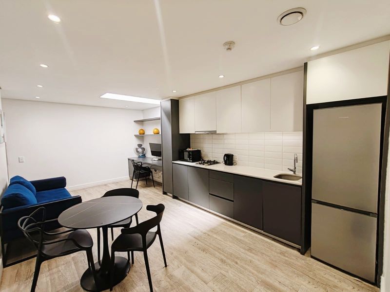 Modern open-plan living area featuring a sleek kitchen with built-in cabinetry, gas cooktop, and integrated workspace, finished with light laminate flooring.