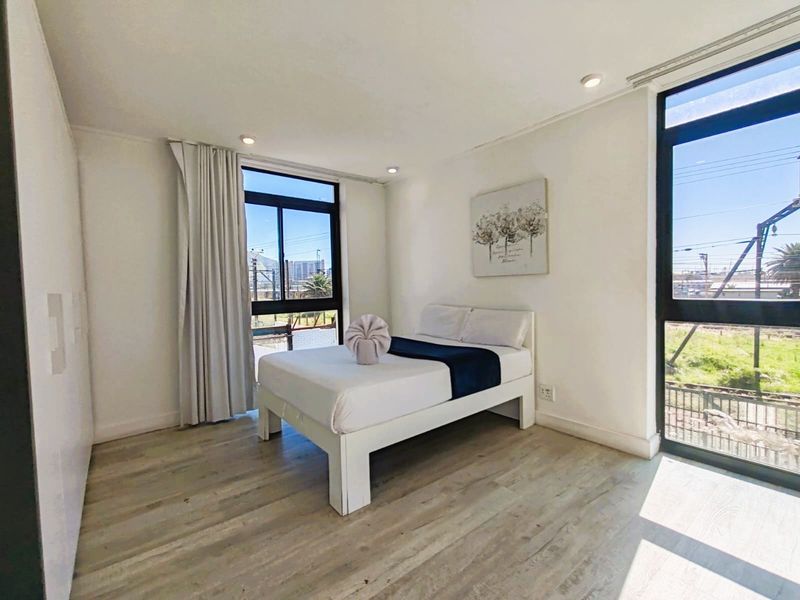 A bright and modern bedroom featuring light laminate flooring, built-in cupboards, and large windows that provide ample natural light.