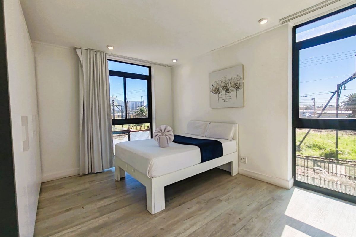 A bright and modern bedroom featuring light laminate flooring, built-in cupboards, and large windows that provide ample natural light.