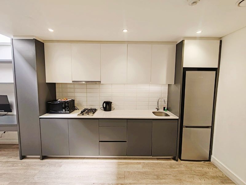Modern compact kitchen featuring two-tone cabinetry, gas hob, extractor fan, subway tile backsplash, and integrated stainless steel sink.