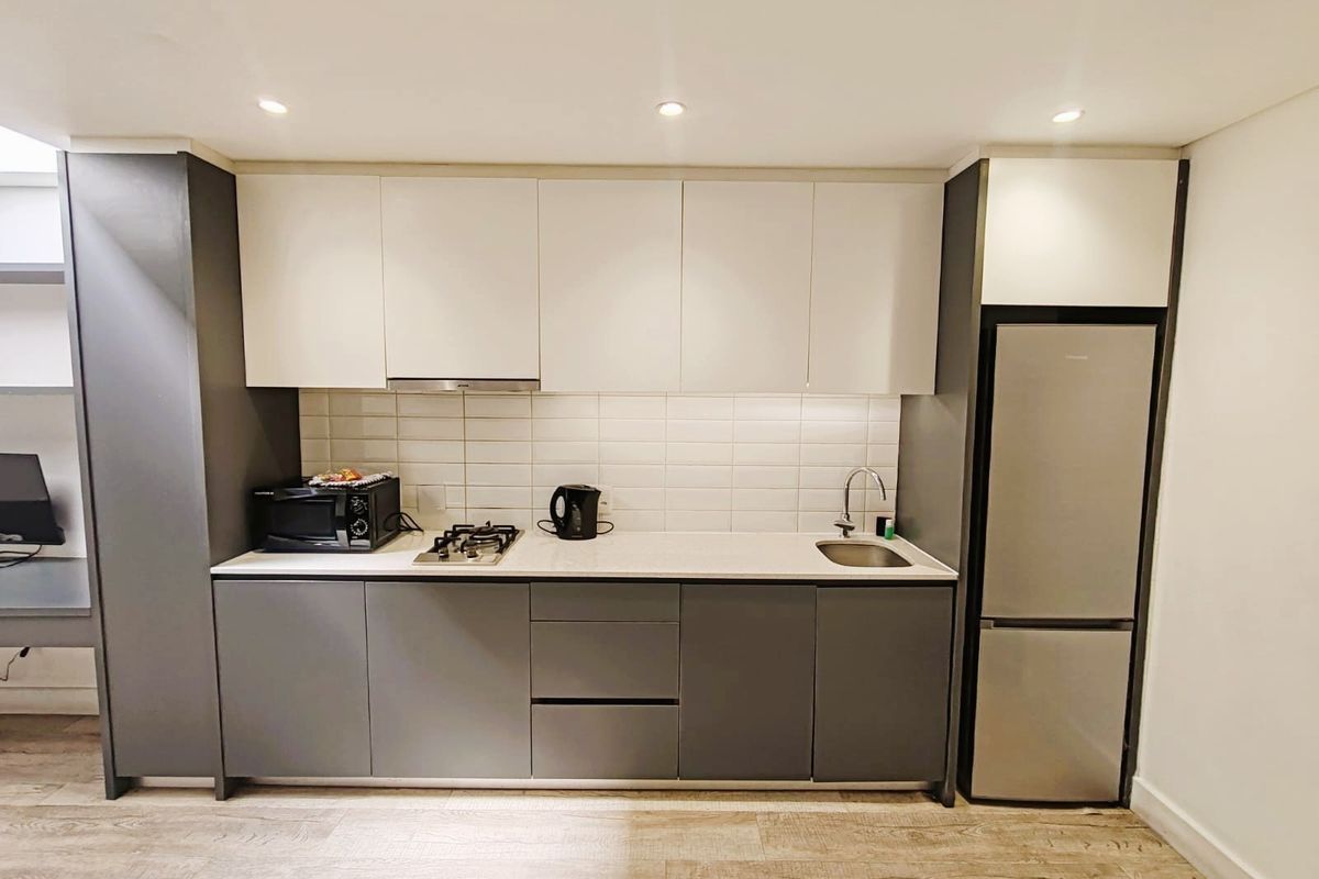 Modern compact kitchen featuring two-tone cabinetry, gas hob, extractor fan, subway tile backsplash, and integrated stainless steel sink.