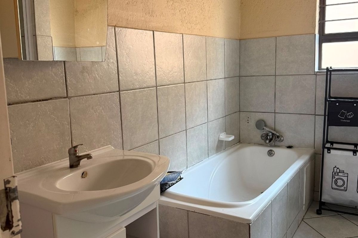 A functional bathroom featuring a tiled bathtub, vanity cabinet with basin, and neutral wall and floor tiling, requiring cosmetic updates to modernize the space.