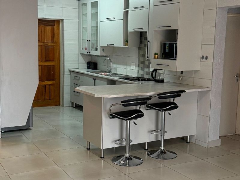 A functional kitchen featuring white built-in cabinetry, a breakfast bar, tiled backsplash, and neutral floor tiles, offering a clean and practical cooking space.