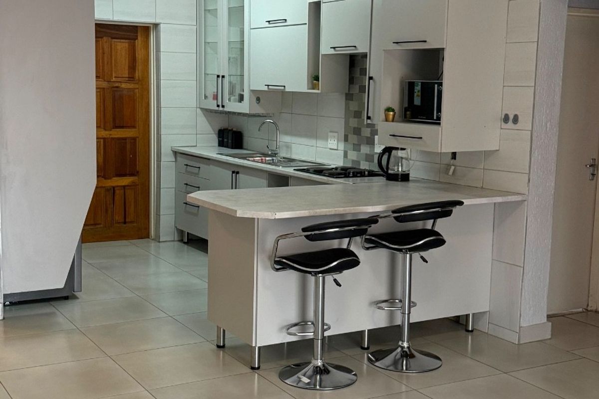 A functional kitchen featuring white built-in cabinetry, a breakfast bar, tiled backsplash, and neutral floor tiles, offering a clean and practical cooking space.