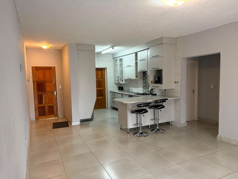 Open plan living area featuring a functional kitchen with built-in cabinetry, a breakfast island, and neutral tiled flooring throughout.