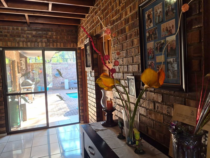 A covered patio area featuring rustic facebrick walls, exposed timber ceiling beams, and tiled flooring, with direct access to the outdoor pool area.