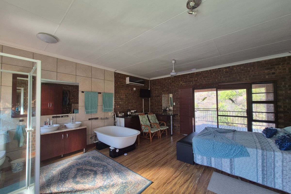 Spacious bedroom featuring an open-plan en-suite with a freestanding bathtub, double vanity, glass shower, exposed brick walls, and sliding doors leading to a balcony.