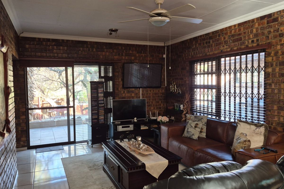 A cozy living room featuring exposed brick walls, tiled flooring, a ceiling fan, and direct access to an outdoor patio area through sliding glass doors.