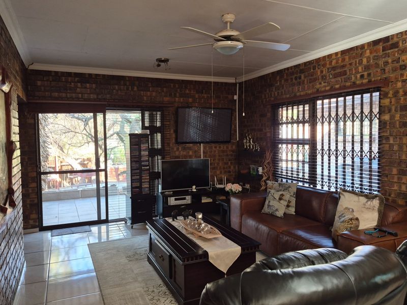 A cozy living room featuring exposed brick walls, tiled flooring, a ceiling fan, and direct access to an outdoor patio area through sliding glass doors.