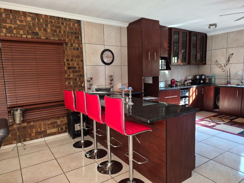 A well-maintained kitchen featuring dark wood cabinetry, granite countertops, a central island with breakfast bar seating, and a distinctive exposed brick feature wall.