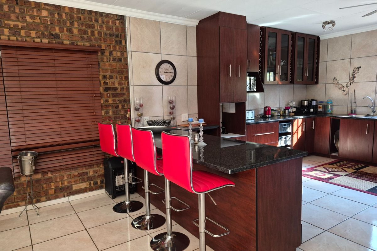 A well-maintained kitchen featuring dark wood cabinetry, granite countertops, a central island with breakfast bar seating, and a distinctive exposed brick feature wall.