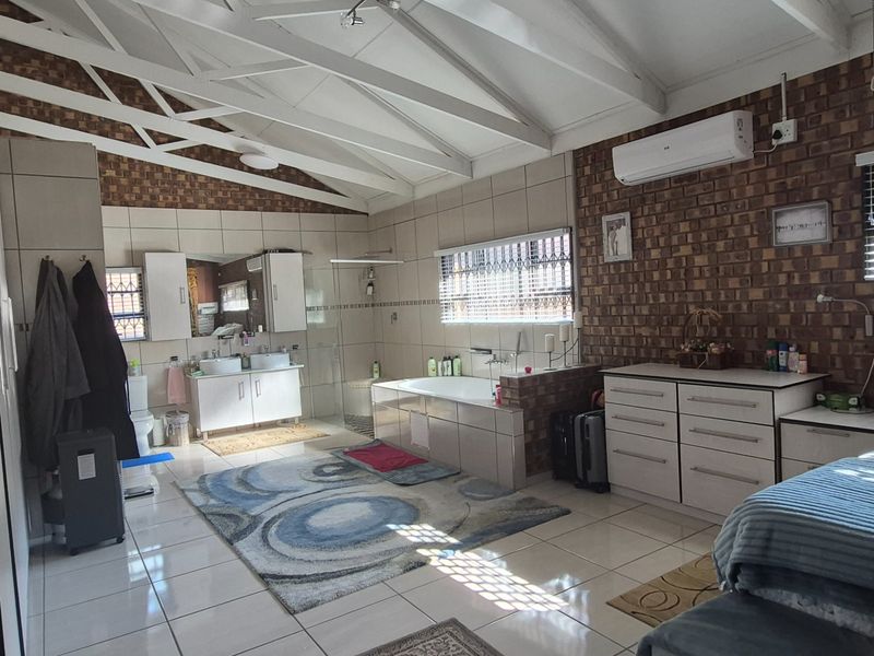 Spacious bathroom featuring a double vanity, built-in bathtub, walk-in shower, and vaulted ceilings with exposed brick accents and tiled flooring.