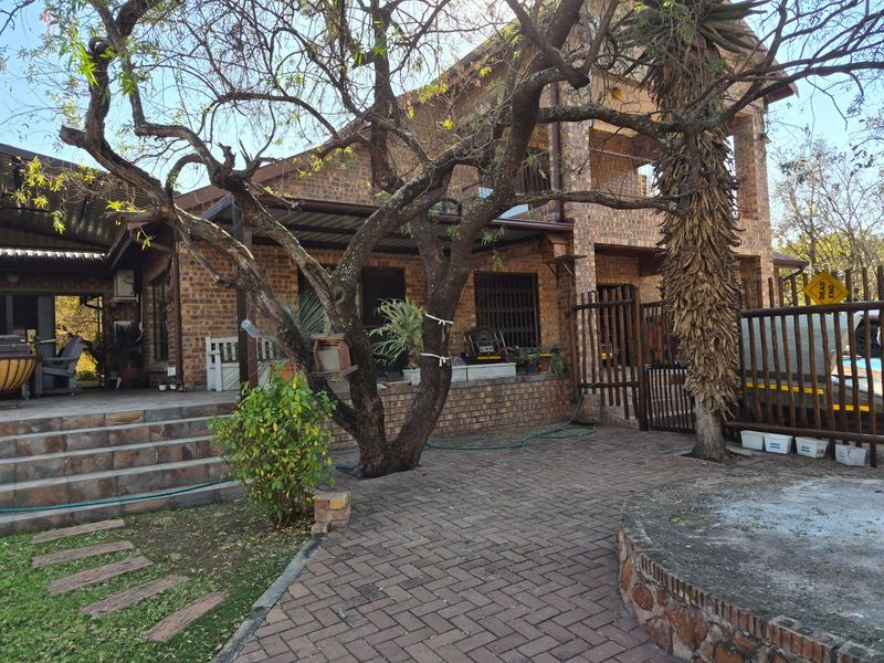 Rear view of a face brick house featuring a paved patio area, covered veranda, and established garden landscaping.