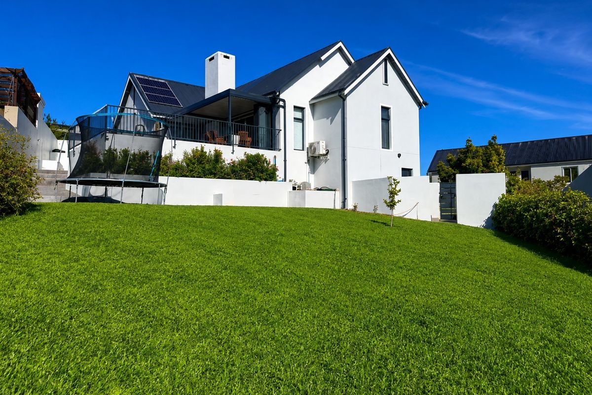 A well-maintained rear exterior view of a modern white house featuring a spacious lawn, balcony, and installed solar panels.