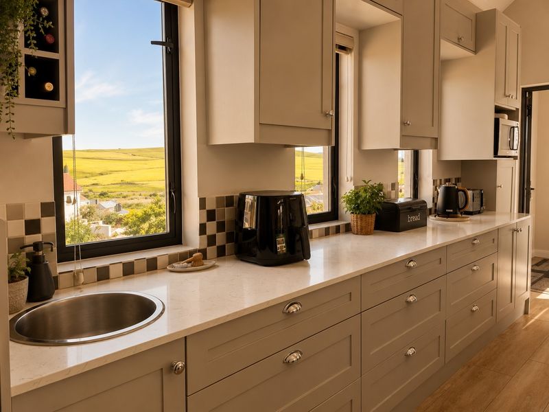 Modern kitchen featuring shaker-style cabinetry, stone countertops, an undermount sink, and a checkered tile backsplash with scenic countryside views.