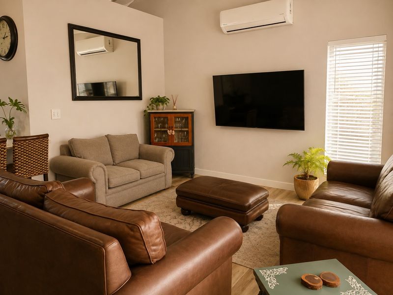 A comfortable living room featuring laminate flooring, a wall-mounted air conditioning unit, and venetian blinds, creating a functional and well-maintained space.