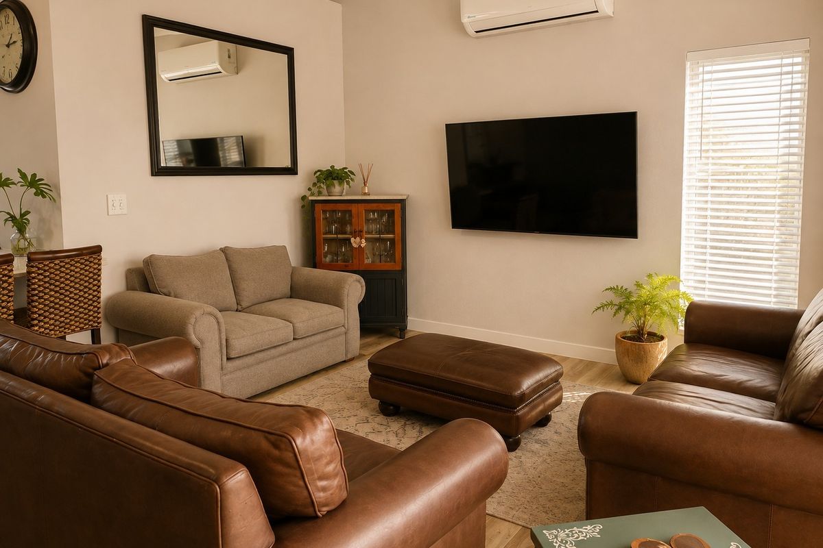 A comfortable living room featuring laminate flooring, a wall-mounted air conditioning unit, and venetian blinds, creating a functional and well-maintained space.
