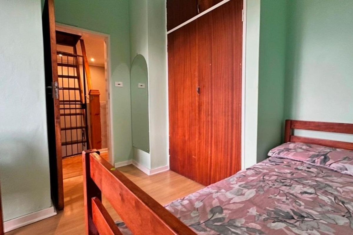 A bedroom featuring laminate flooring, a built-in wooden wardrobe, and an arched wall mirror, with a view into an adjacent hallway.