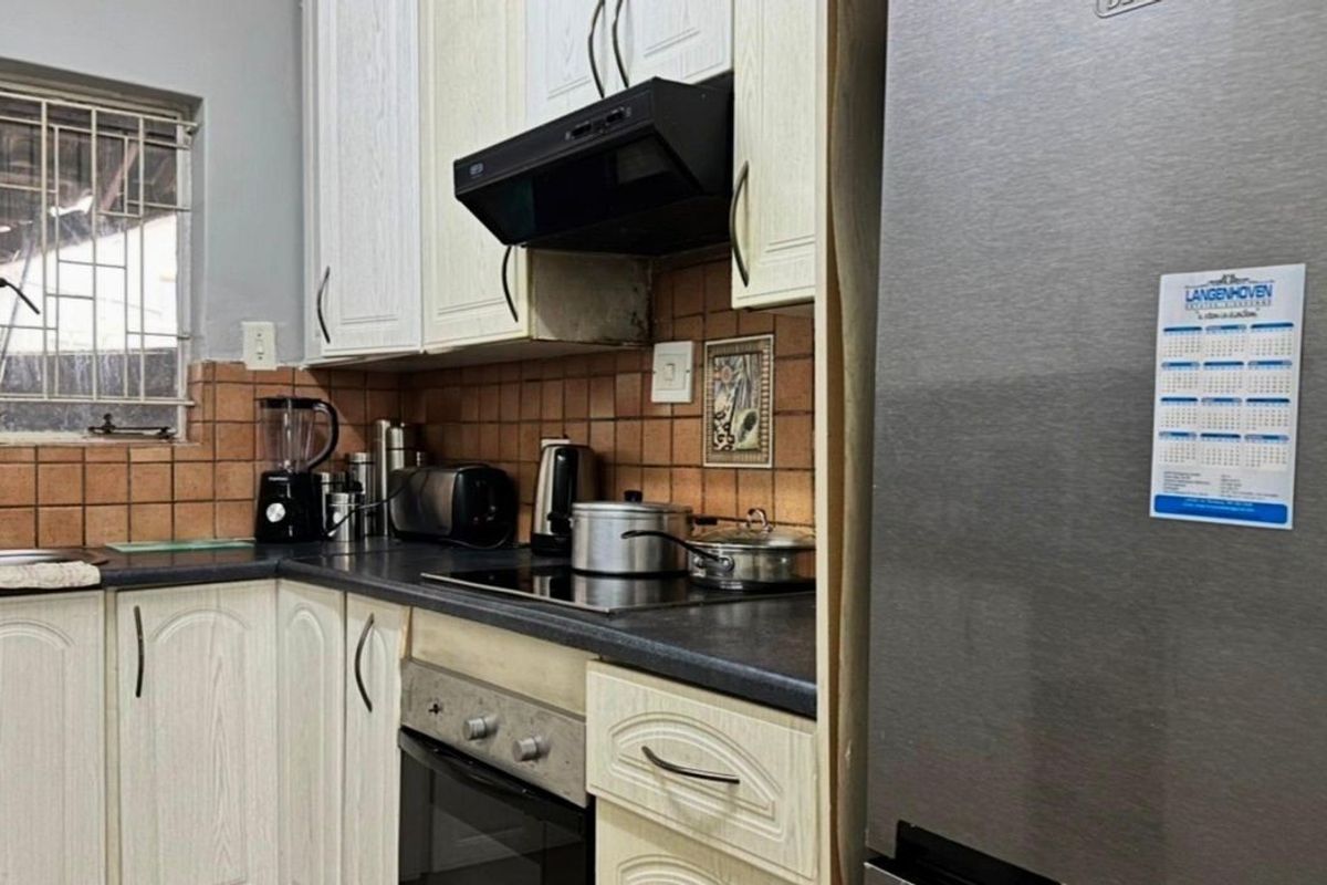 A functional kitchen featuring built-in cabinetry, dark laminate countertops, an electric hob with extractor fan, and a tiled backsplash.