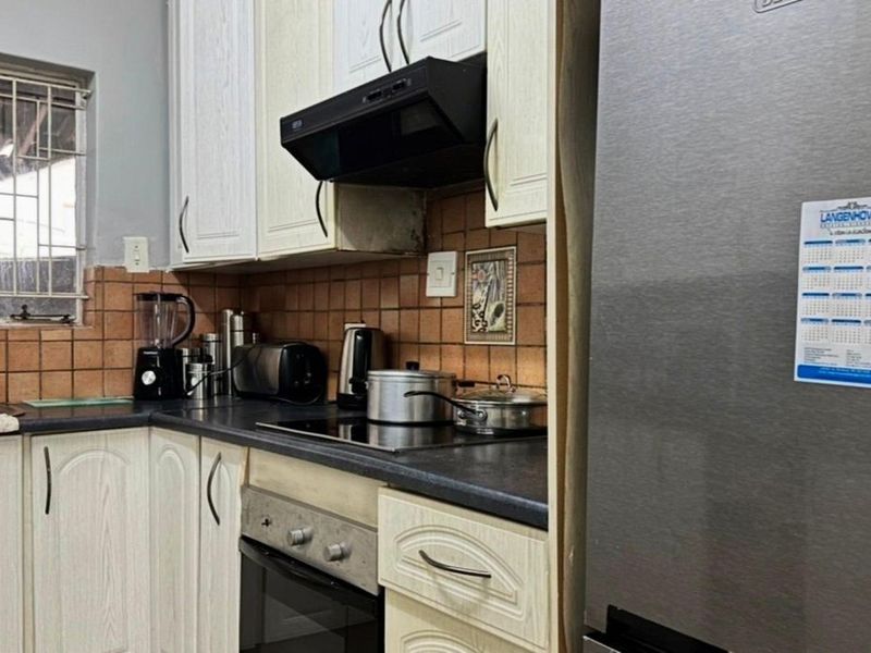 A functional kitchen featuring built-in cabinetry, dark laminate countertops, an electric hob with extractor fan, and a tiled backsplash.