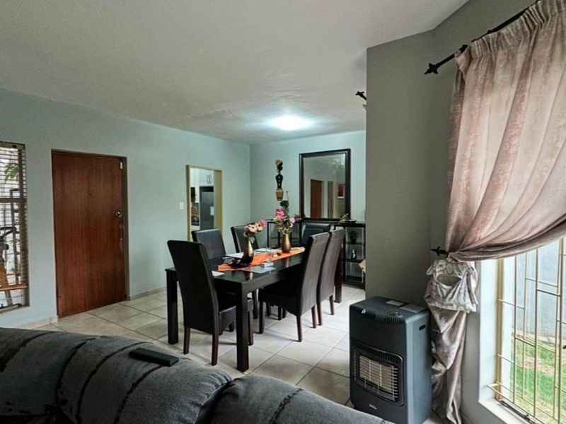 Dining area featuring tiled flooring and access to an adjacent room, with natural light provided by a large window with security bars.
