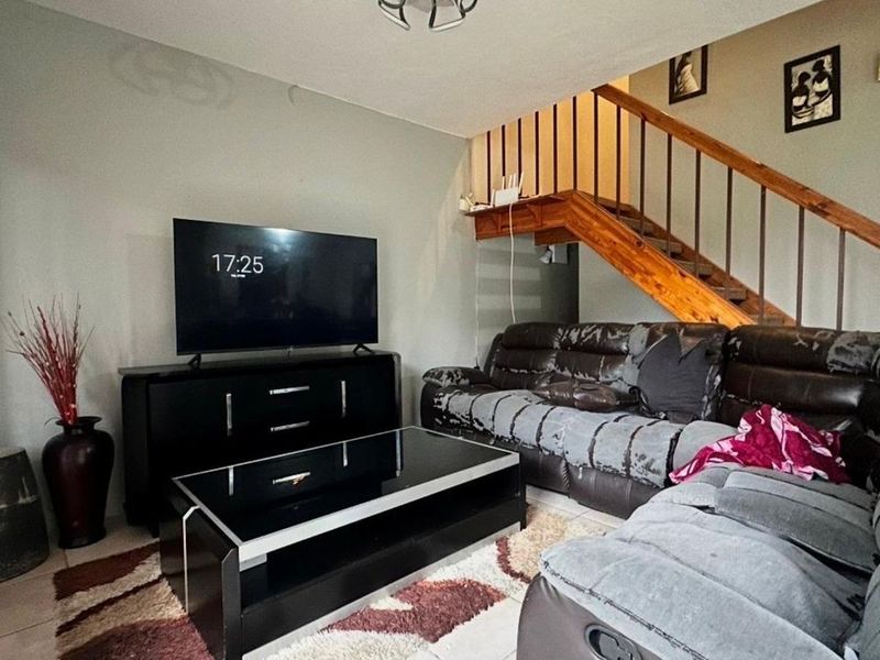 A living room area featuring tiled flooring and an open wooden staircase leading to the upper level.