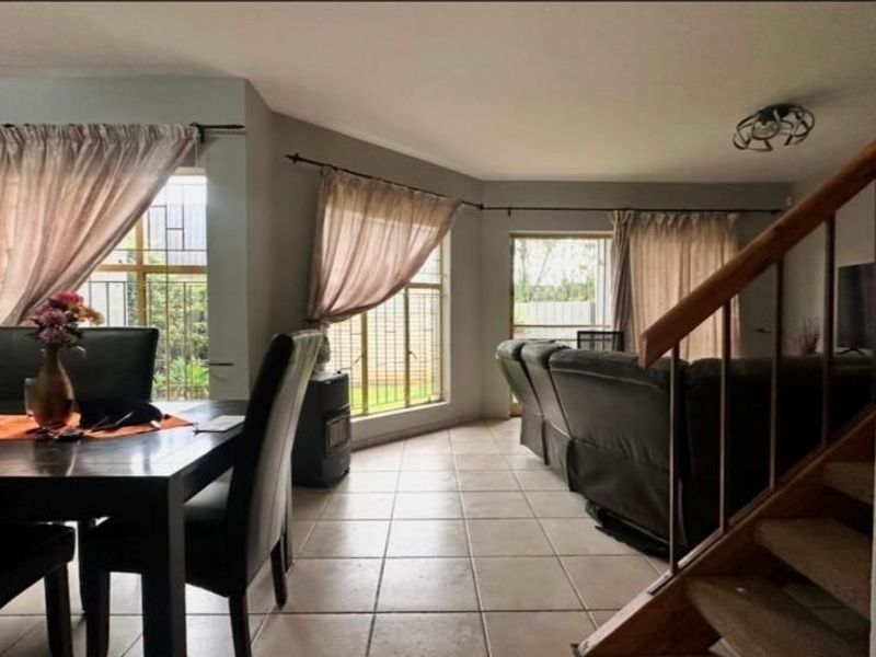 Open plan living and dining area featuring ceramic floor tiles, a wooden staircase, and large windows with security bars.