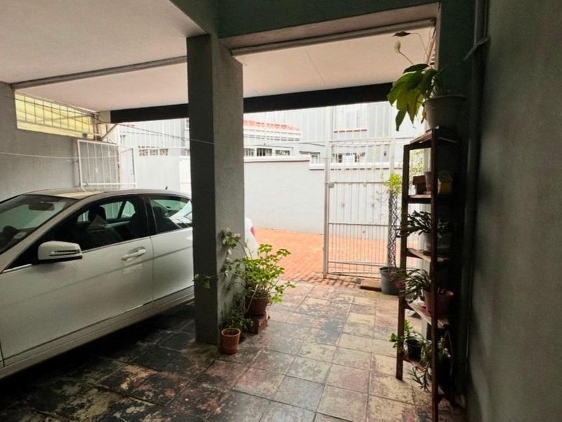 A covered garage area featuring tiled flooring, a structural concrete pillar, and a metal security gate leading to the exterior.