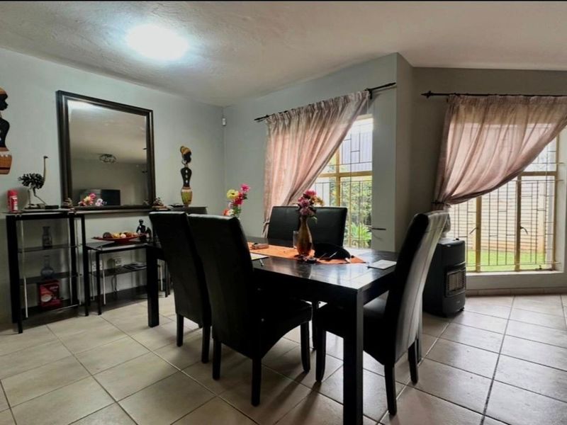 A dining room featuring tiled flooring and large windows fitted with security bars, providing natural light to the space.