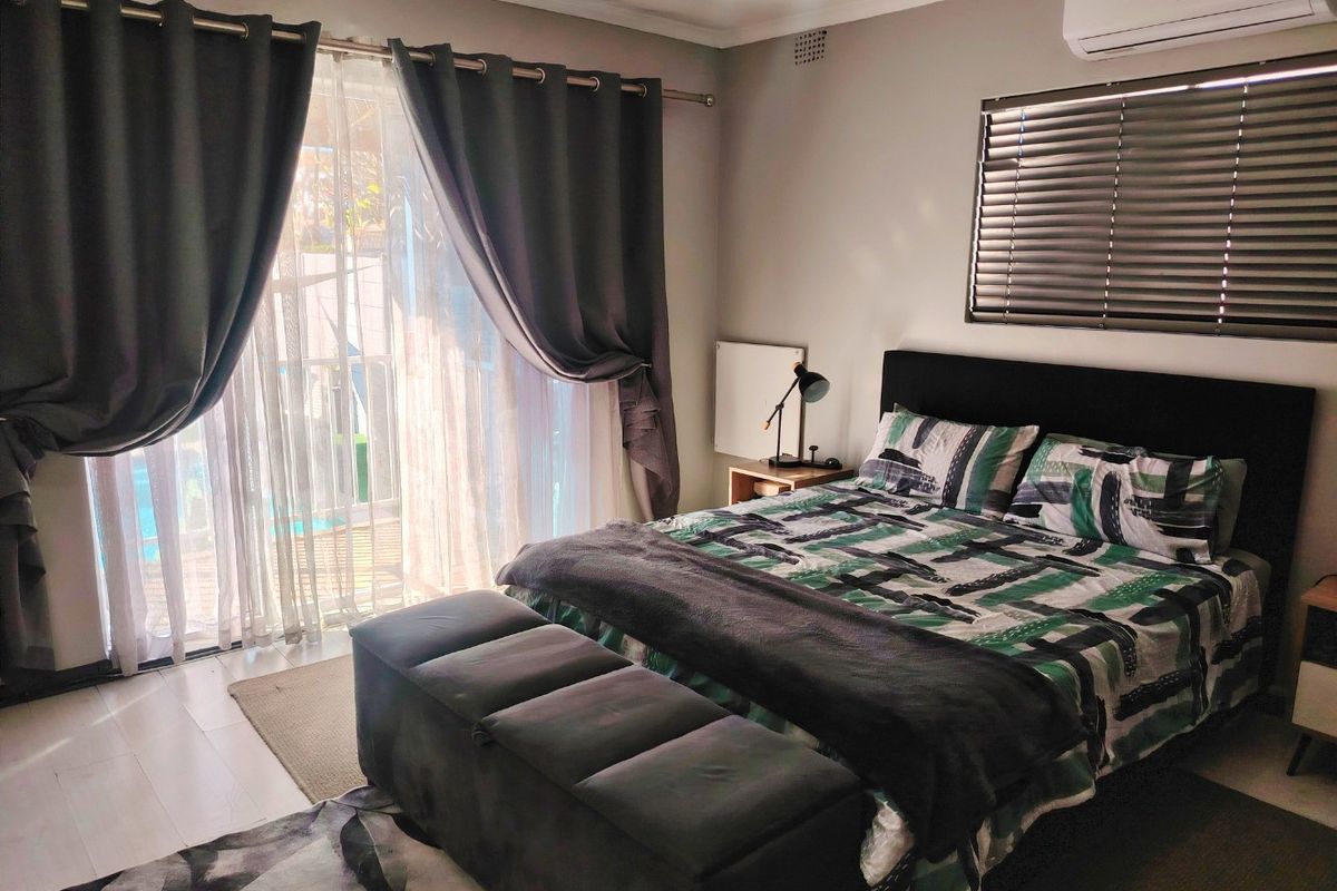 A well-maintained bedroom featuring a split-system air conditioner, venetian blinds, and a sliding glass door providing access to the outdoor area.